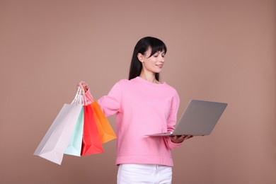 Photo of Internet shopping. Happy woman with laptop and colorful bags on beige background