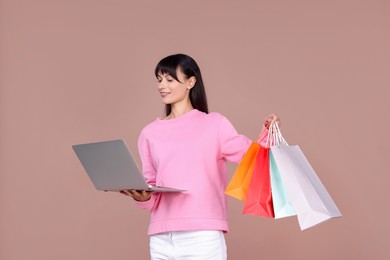 Photo of Internet shopping. Happy woman with laptop and colorful bags on beige background