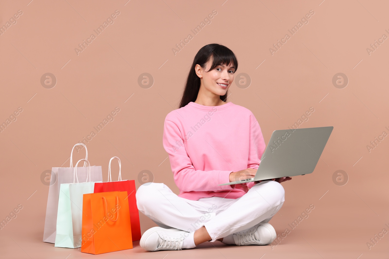 Photo of Internet shopping. Happy woman with laptop and colorful bags on beige background