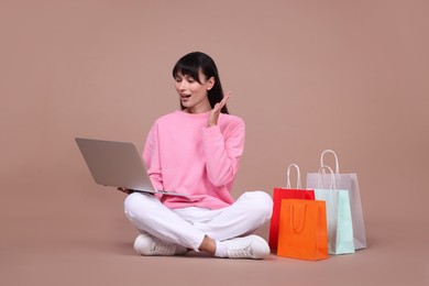 Photo of Internet shopping. Surprised woman with laptop and colorful bags on beige background