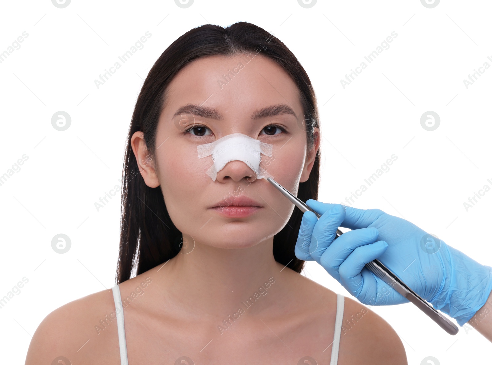 Photo of Doctor removing medical bandage from patient's nose after plastic surgery operation on white background, closeup