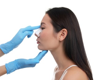 Doctor checking patient's nose after plastic surgery operation on white background, closeup