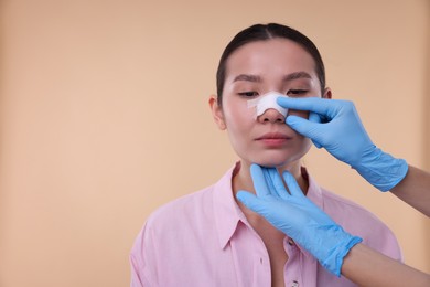 Photo of Doctor checking patient's nose after plastic surgery operation on beige background, closeup. Space for text