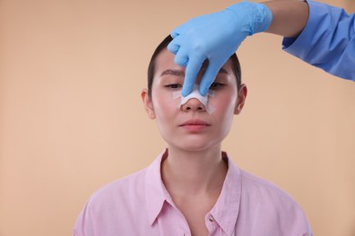 Photo of Doctor checking patient's nose after plastic surgery operation on beige background, closeup