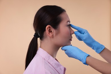 Photo of Doctor checking patient's nose before plastic surgery operation on beige background, closeup