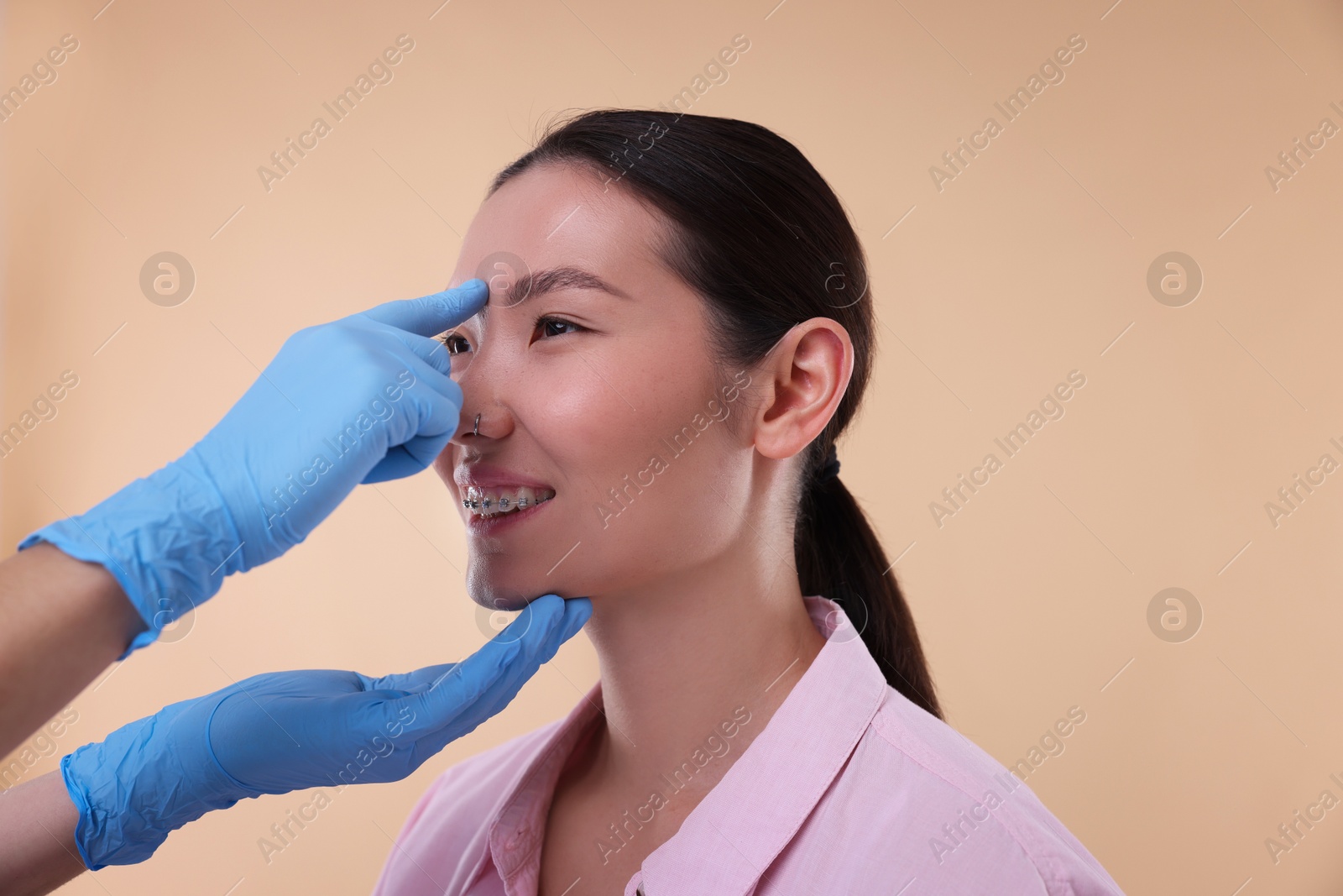 Photo of Doctor checking patient's nose before plastic surgery operation on beige background, closeup