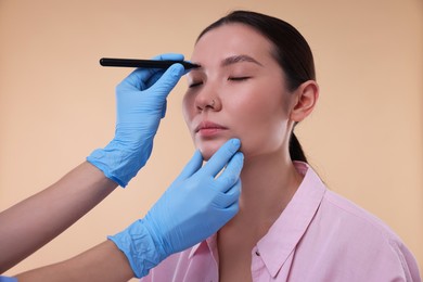 Photo of Doctor drawing marks on patient's nose for plastic surgery operation against beige background, closeup