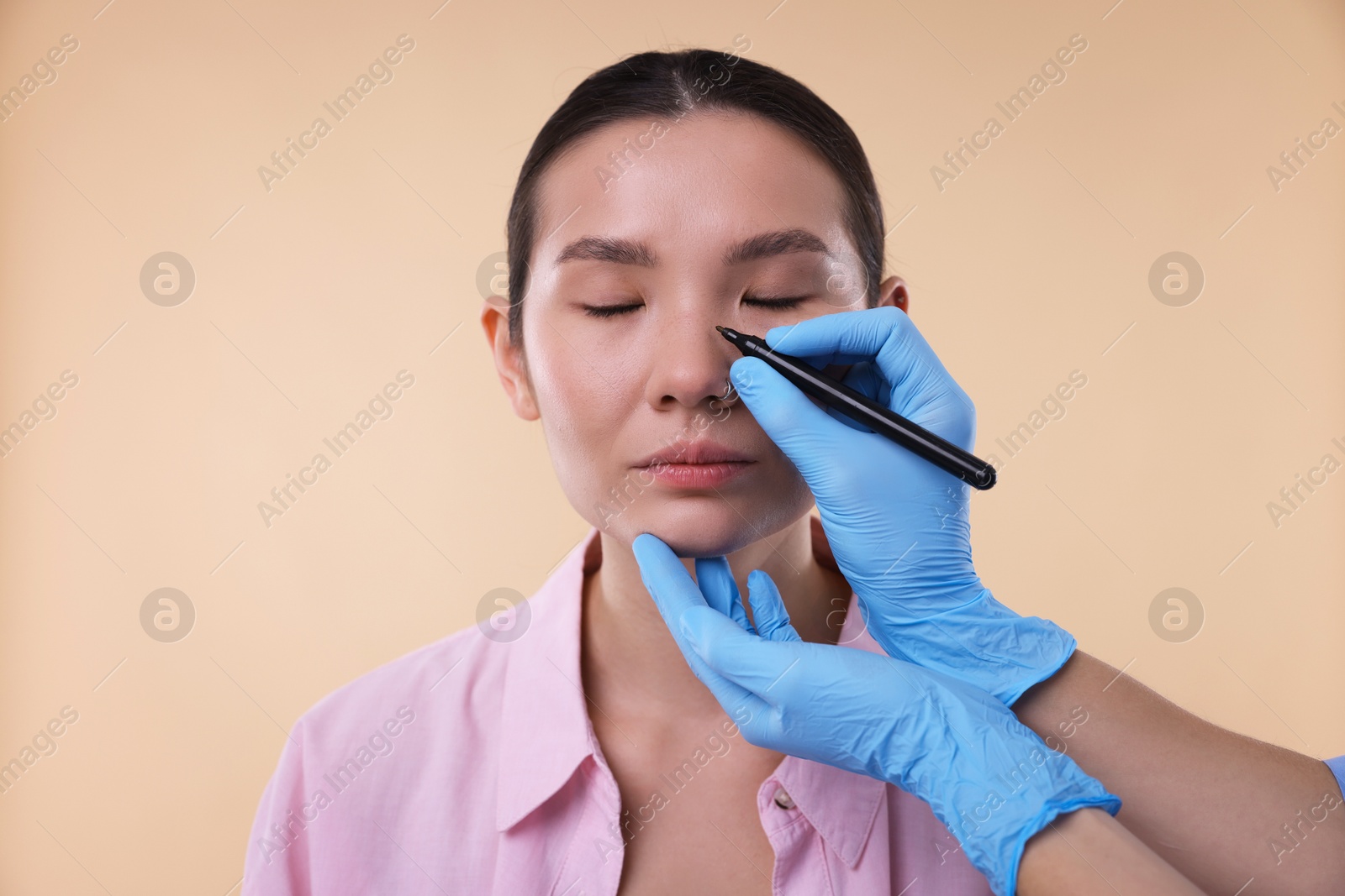 Photo of Doctor drawing marks on patient's nose for plastic surgery operation against beige background, closeup