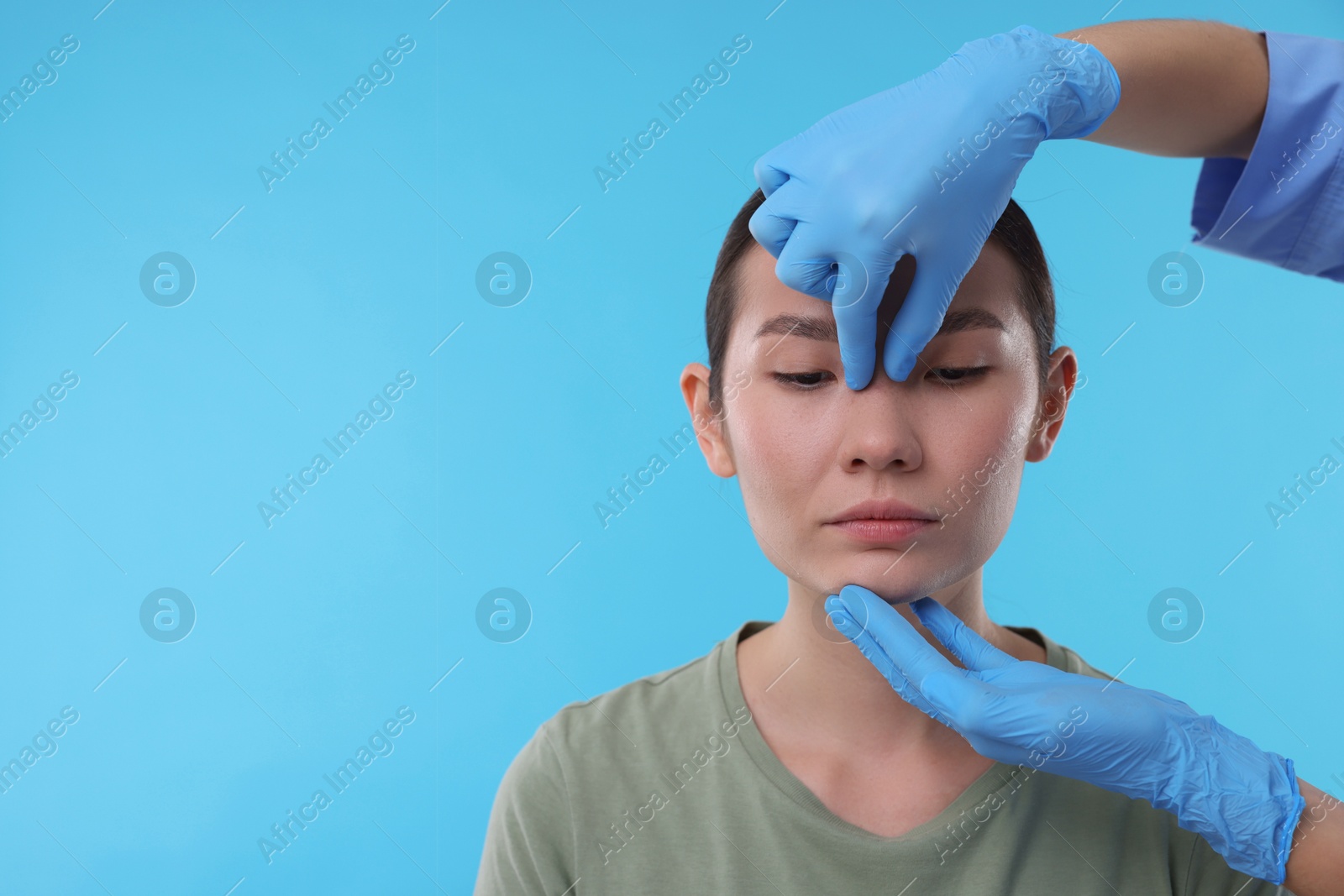 Photo of Doctor checking patient's nose before plastic surgery operation on light blue background, closeup. Space for text