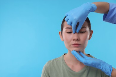 Doctor checking patient's nose before plastic surgery operation on light blue background, closeup. Space for text