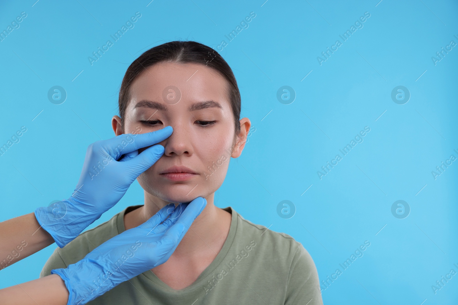 Photo of Doctor checking patient's nose before plastic surgery operation on light blue background, closeup. Space for text