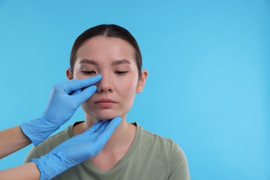 Photo of Doctor checking patient's nose before plastic surgery operation on light blue background, closeup. Space for text