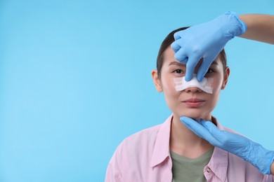 Photo of Doctor checking patient's nose after plastic surgery operation on light blue background, closeup. Space for text