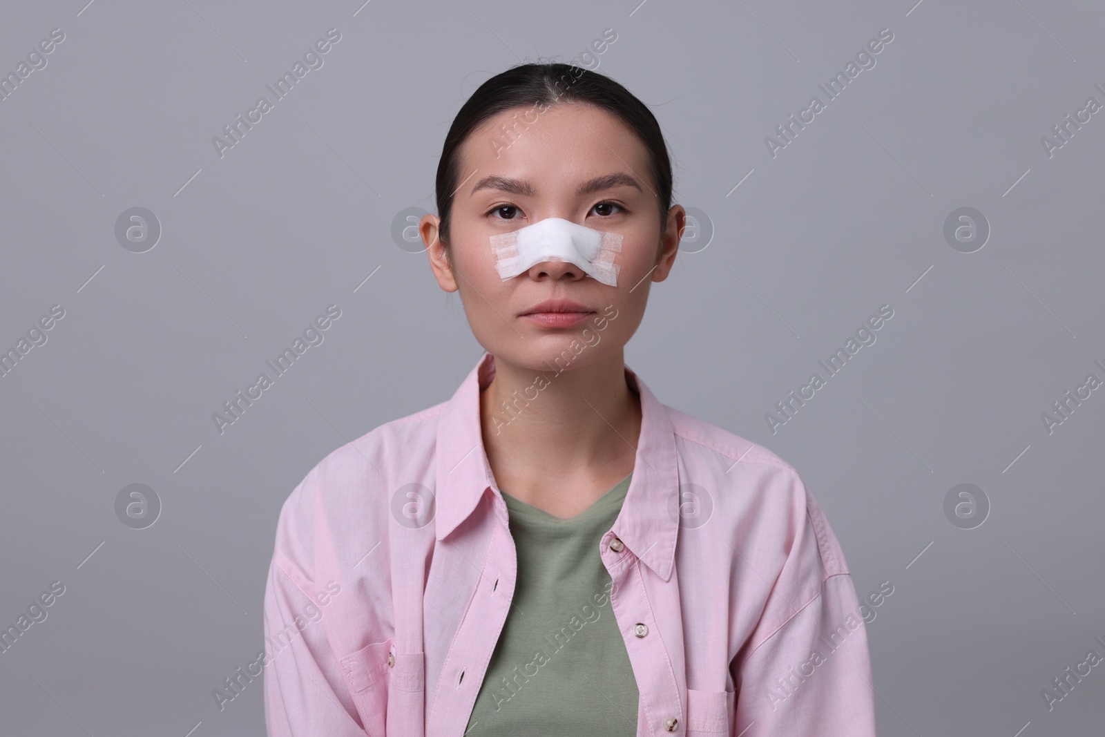 Photo of Woman with medical bandage on her nose after plastic surgery operation against light grey background