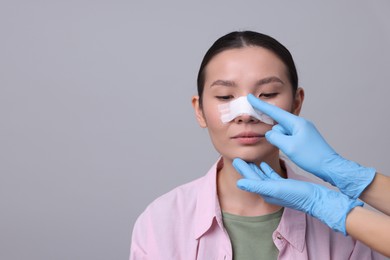 Photo of Doctor checking patient's nose after plastic surgery operation on light grey background, closeup. Space for text