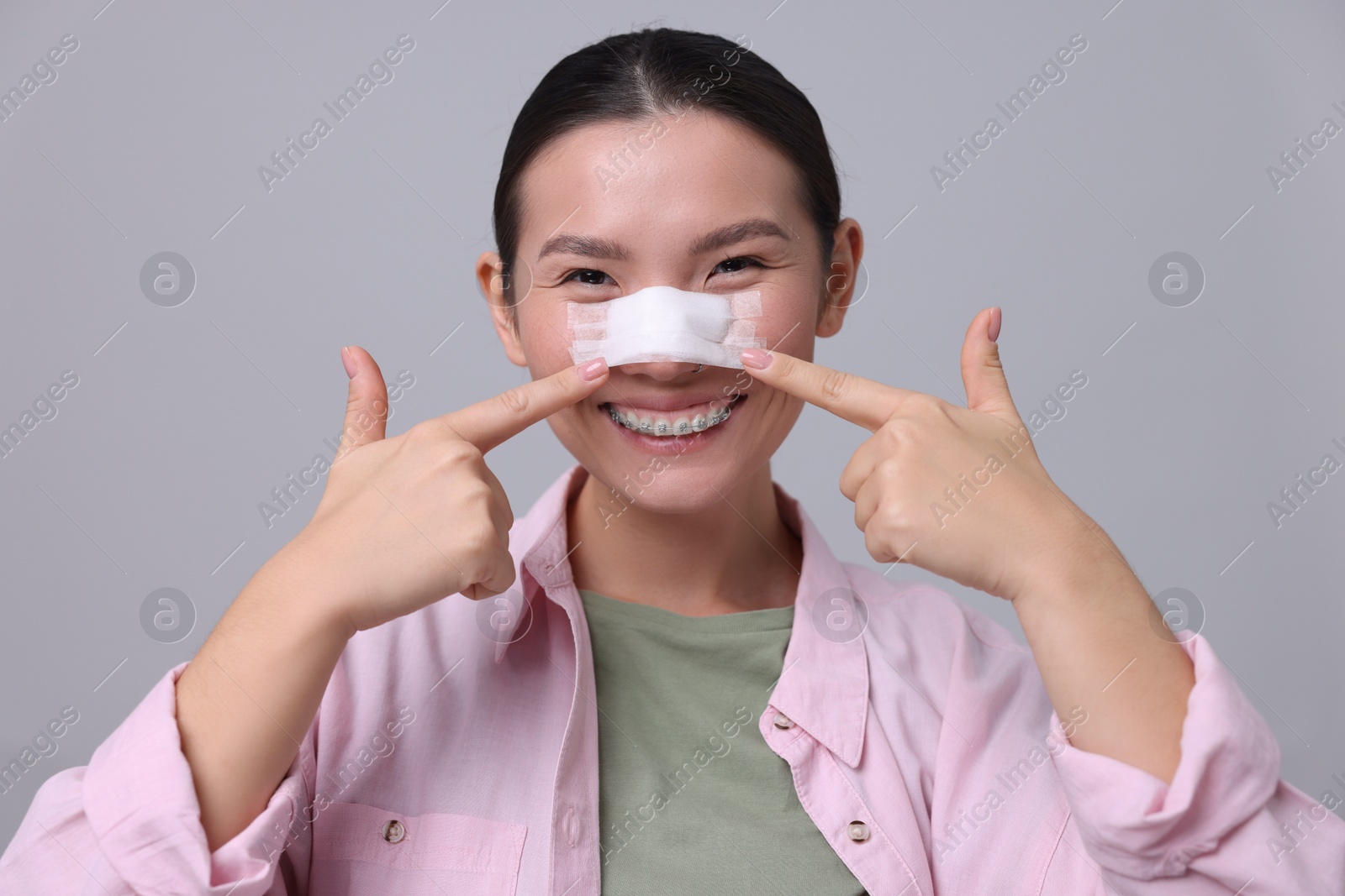 Photo of Woman with medical bandage on her nose after plastic surgery operation against light grey background