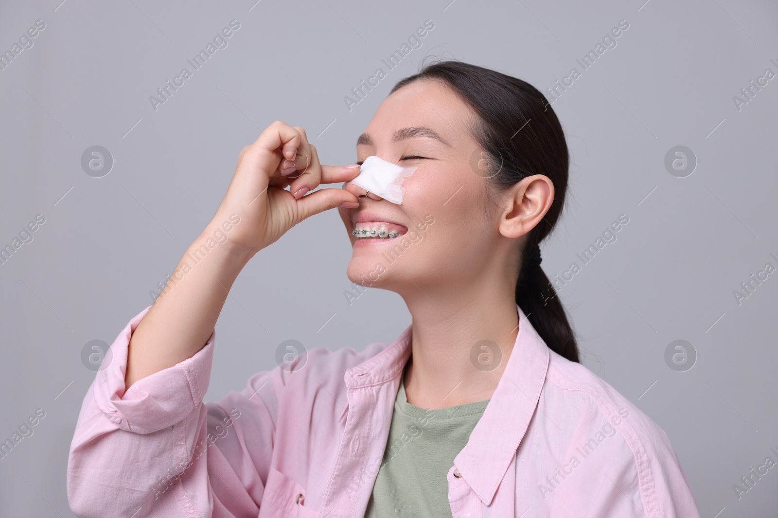 Photo of Woman with medical bandage on her nose after plastic surgery operation against light grey background