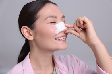 Photo of Woman with medical bandage on her nose after plastic surgery operation against light grey background, closeup