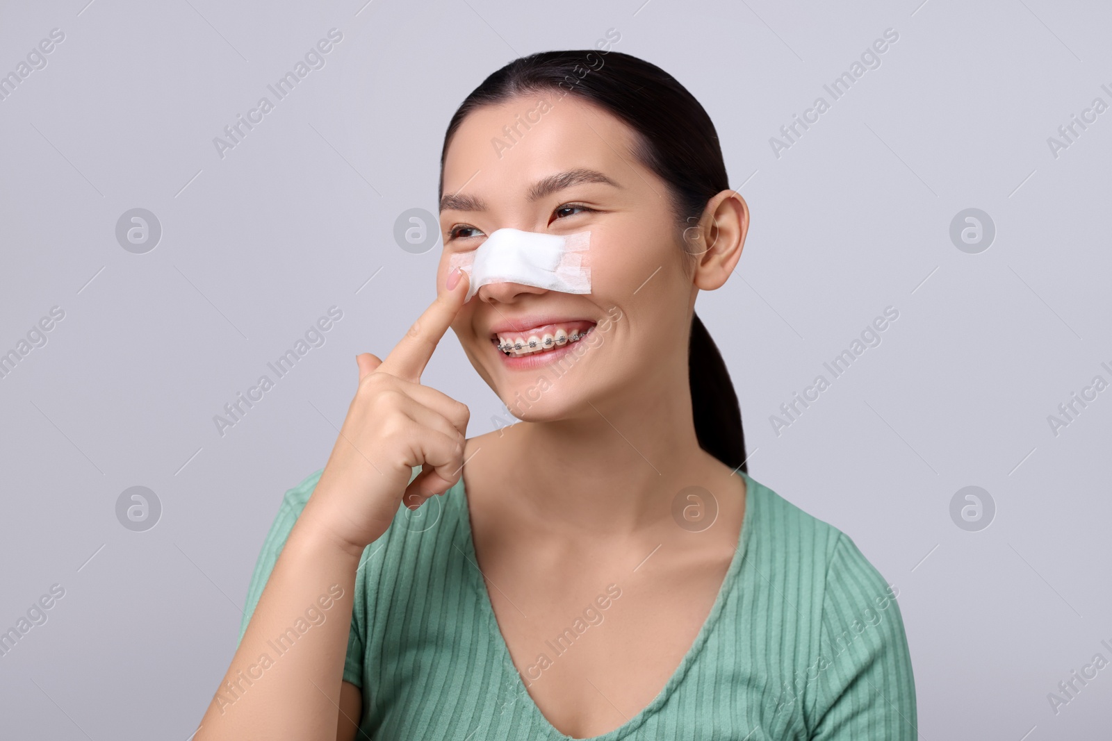 Photo of Woman with medical bandage on her nose after plastic surgery operation against light grey background. Space for text