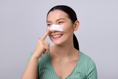 Photo of Woman with medical bandage on her nose after plastic surgery operation against light grey background. Space for text