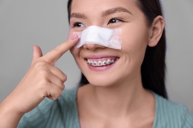 Photo of Woman with medical bandage on her nose after plastic surgery operation against light grey background, closeup