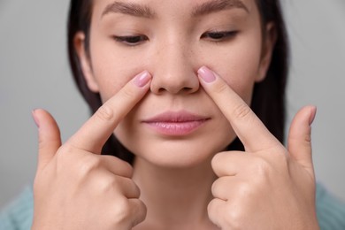 Photo of Woman touching her nose on light grey background, closeup