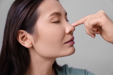 Photo of Woman touching her nose on light grey background, closeup