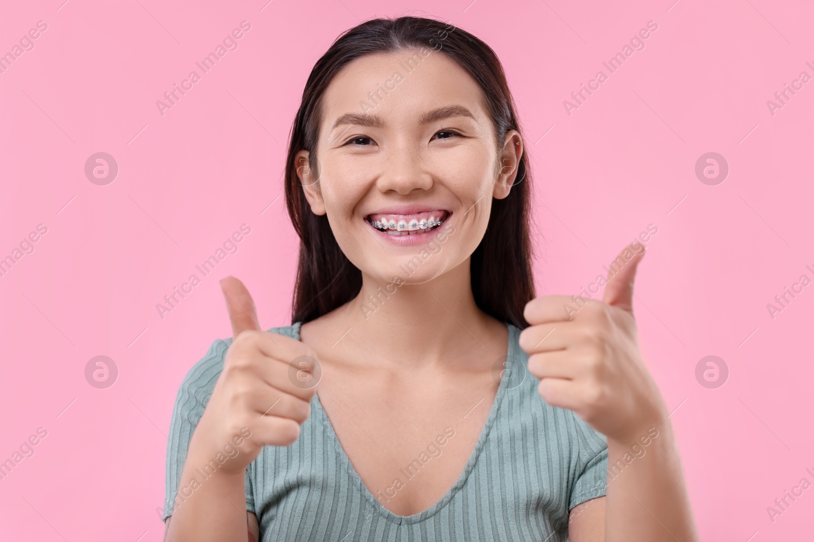 Photo of Woman with beautiful nose showing thumbs up on pink background. Rhinoplasty surgery