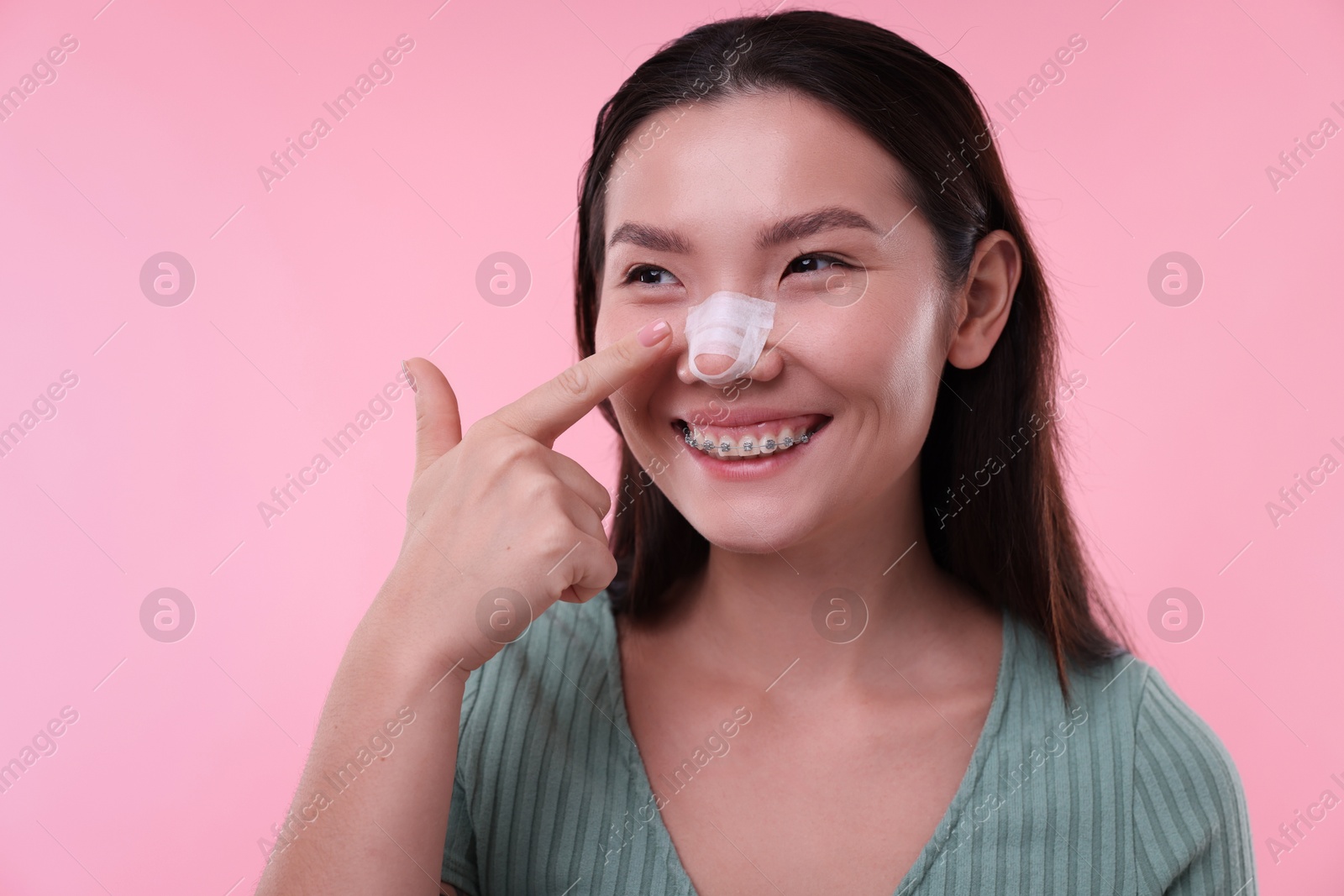 Photo of Woman with medical bandage on her nose after plastic surgery operation against pink background