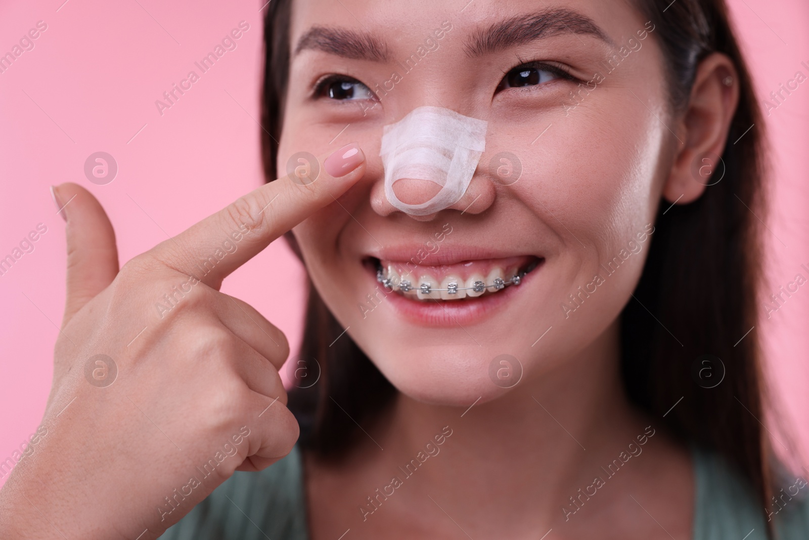 Photo of Woman with medical bandage on her nose after plastic surgery operation against pink background, closeup