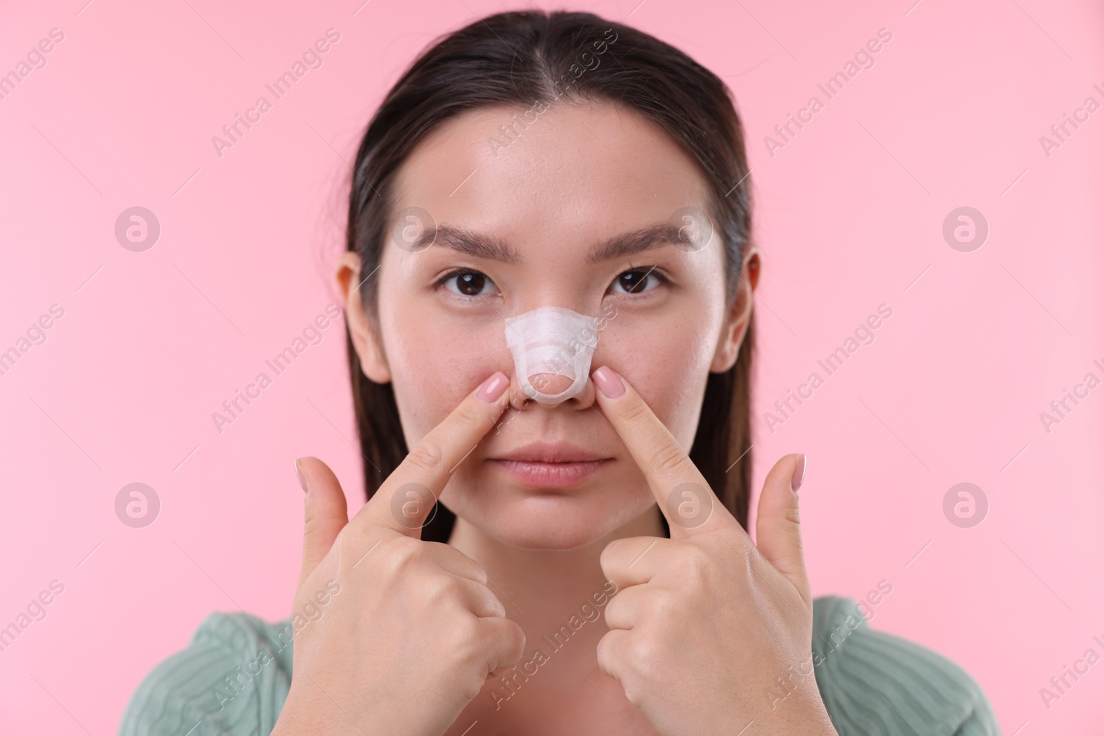 Photo of Woman with medical bandage on her nose after plastic surgery operation against pink background