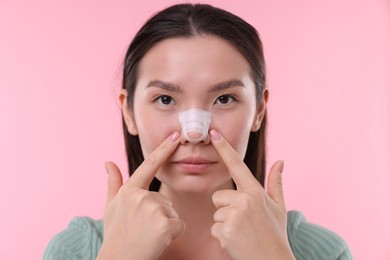 Woman with medical bandage on her nose after plastic surgery operation against pink background