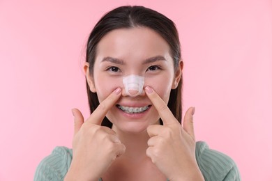 Photo of Woman with medical bandage on her nose after plastic surgery operation against pink background