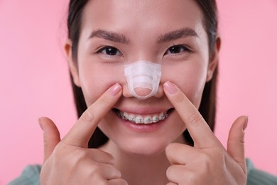 Photo of Woman with medical bandage on her nose after plastic surgery operation against pink background, closeup