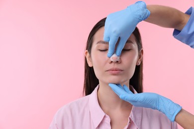 Doctor checking patient's nose after plastic surgery operation on pink background, closeup. Space for text