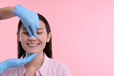 Photo of Doctor checking patient's nose after plastic surgery operation on pink background, closeup. Space for text