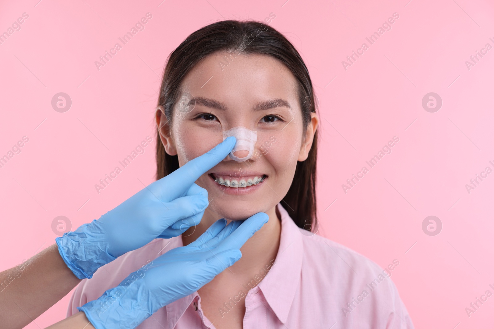 Photo of Doctor checking patient's nose after plastic surgery operation on pink background, closeup