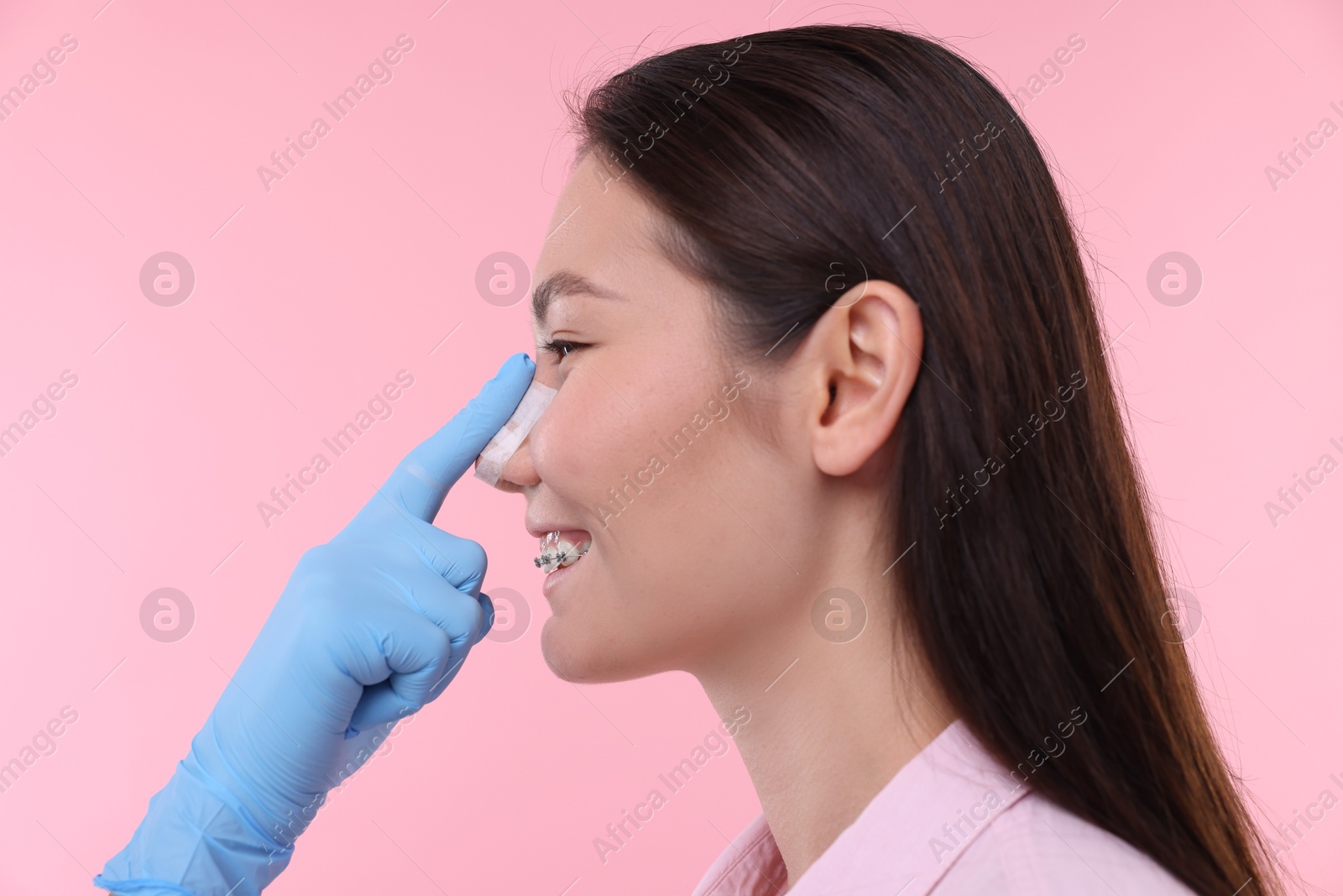 Photo of Doctor checking patient's nose after plastic surgery operation on pink background, closeup