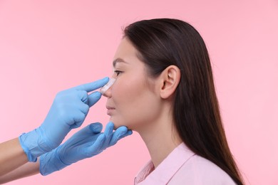 Photo of Doctor checking patient's nose after plastic surgery operation on pink background, closeup