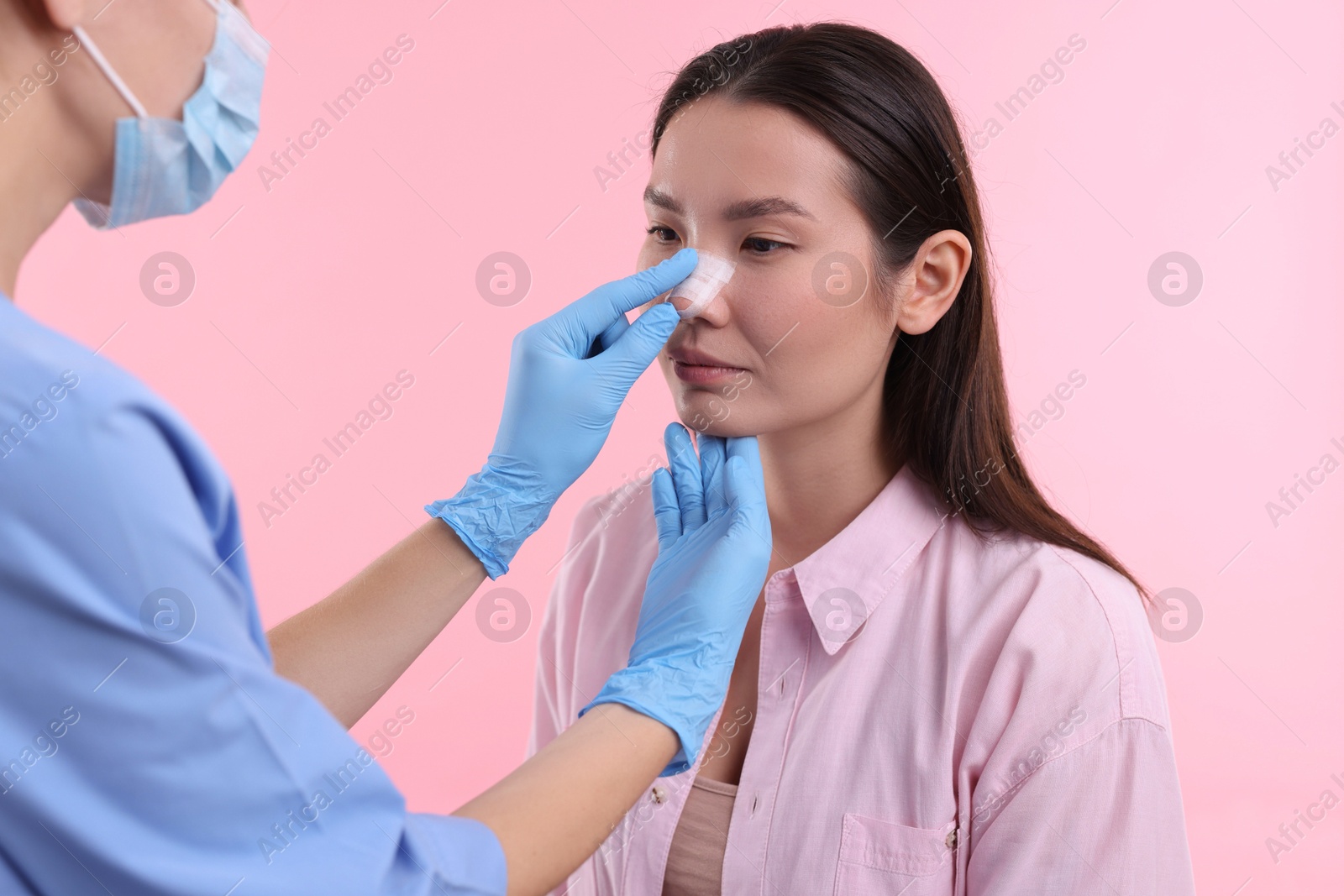 Photo of Doctor checking patient's nose after plastic surgery operation on pink background