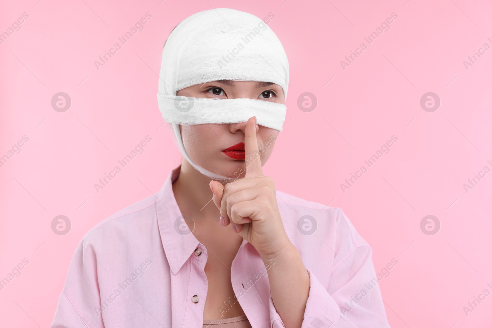 Photo of Woman with nose wrapped in medical bandage after plastic surgery operation making silent gesture on pink background