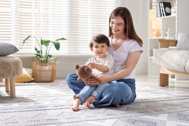 Photo of Happy mother and her cute little son with toy bear on carpet at home