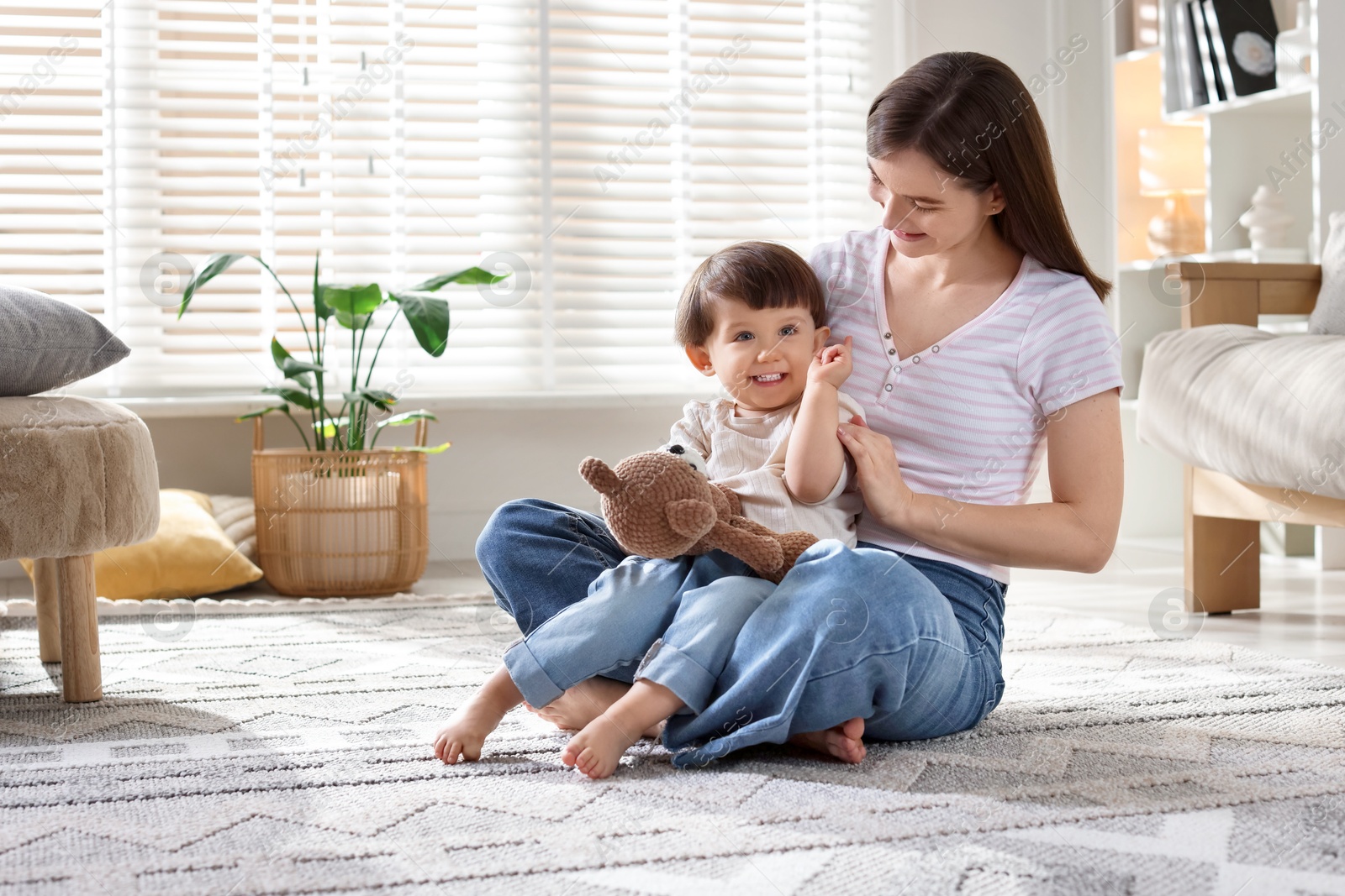 Photo of Happy mother and her cute little son with toy bear on carpet at home