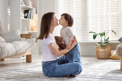 Photo of Happy mother and her cute little son with toy bear on carpet at home