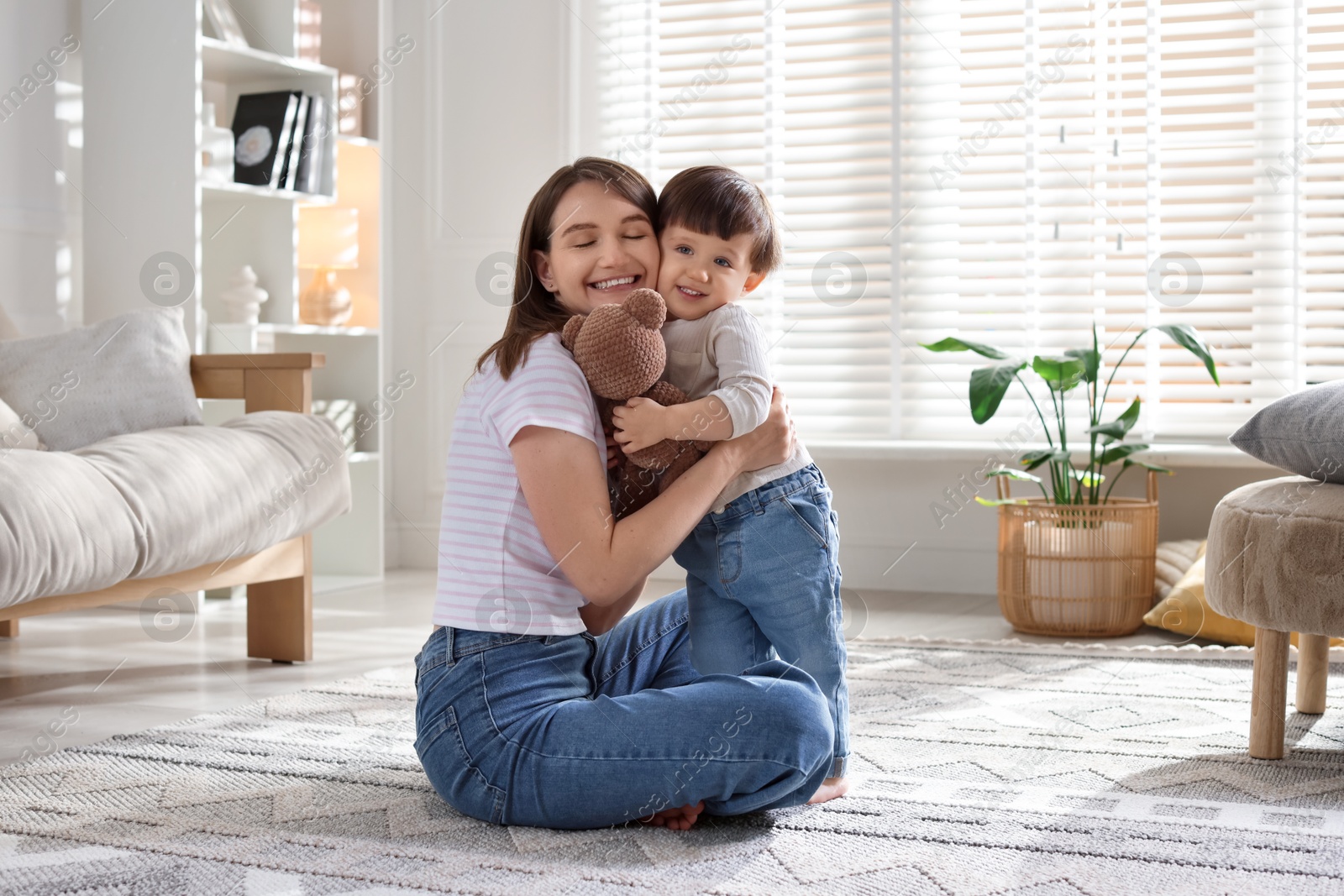 Photo of Happy mother and her cute little son with toy bear on carpet at home