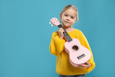 Photo of Little girl with ukulele on light blue background, space for text