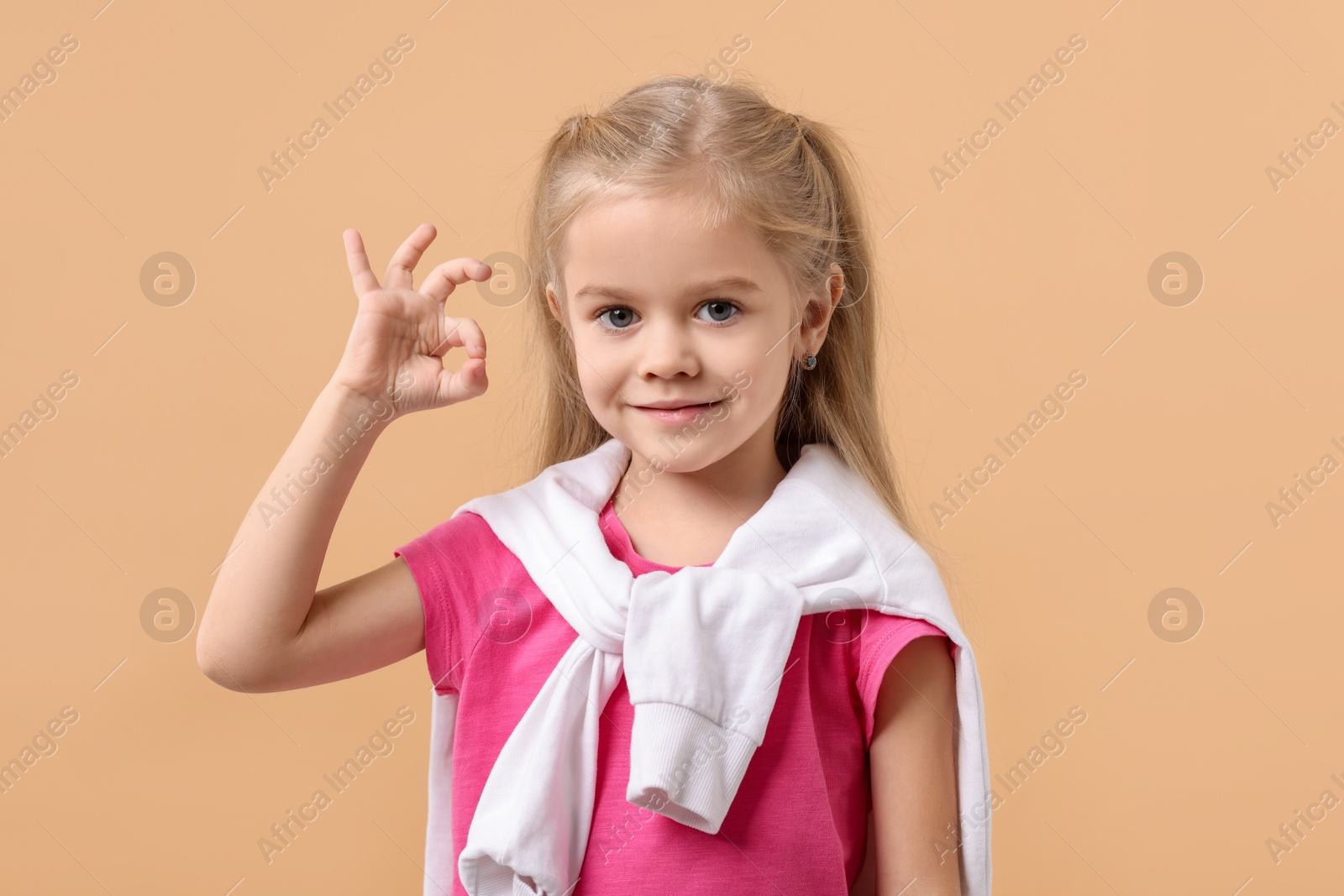 Photo of Cute little girl showing OK gesture on beige background