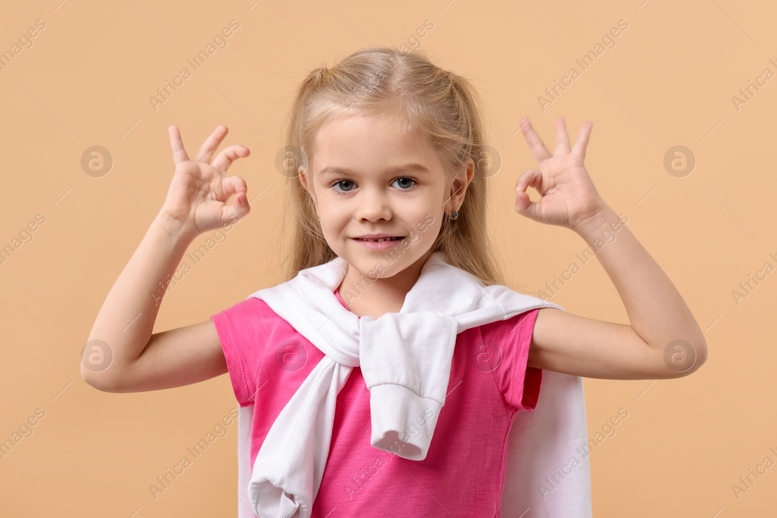 Photo of Cute little girl showing OK gesture on beige background