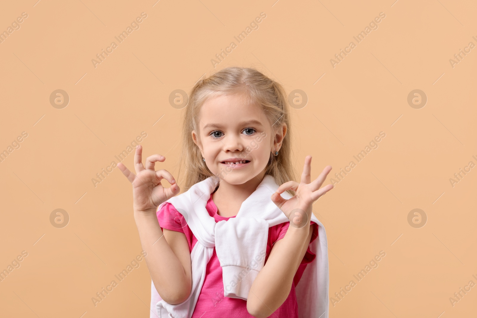 Photo of Cute little girl showing OK gesture on beige background