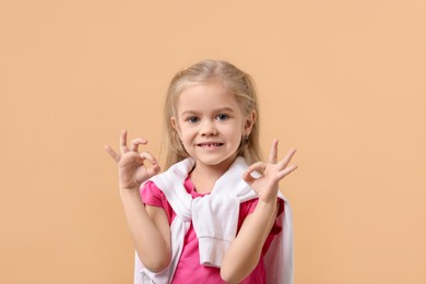 Photo of Cute little girl showing OK gesture on beige background